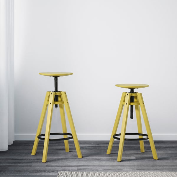 Two yellow adjustable bar stools, suitable for heights 90-110 cm, placed against a white wall on a grey floor.
