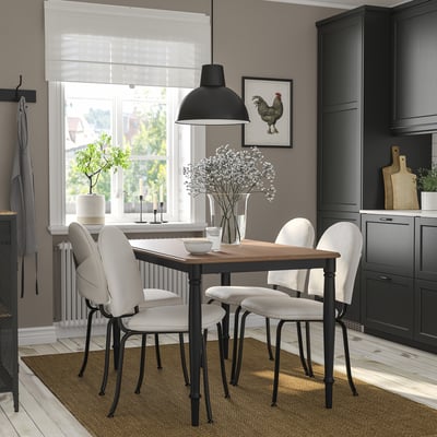 Modern dining set with black metal legs & wooden top, four white chairs, hanging light, gray walls, large window.