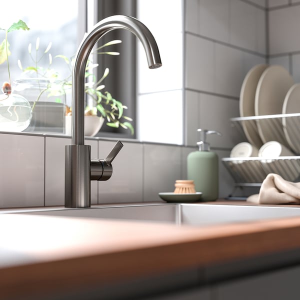 Modern kitchen with DELSJÖN pewter tap, sleek design, tall spout, surrounded by green soap dispenser and plates, set against grey tiles.