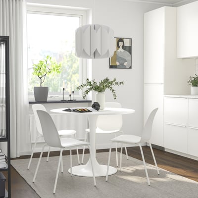 Modern dining setup with white DOCKSTA table, four chairs, metal base, pendant light, plants, and picture in minimalist room.