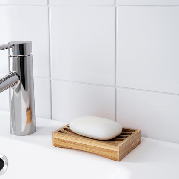 Modern bathroom sink with chrome faucet, bamboo soap dish, and white soap on a white countertop and tiled wall.
