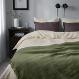 Grey-green throw DYTÅG with purple cushions and flowers.