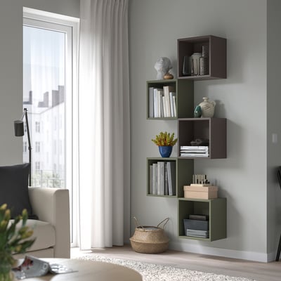 Wall-mounted EKET shelves in green & brown, holding books, plants & decor. Beside a large window with white curtains, it adds modern storage & style.