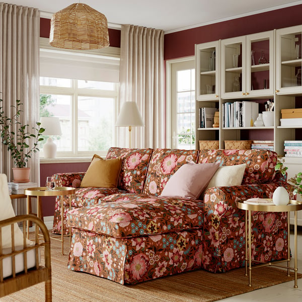 Cosy living room with large floral-patterned brown & pink EKTORP sofa, matching armchair, and view of bookcase. .