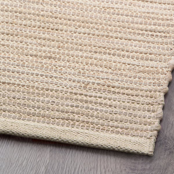 Handwoven cotton rug, neutral tones, textured weave, soft surface, finely stitched edges.