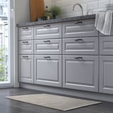 Modern kitchen with gray cabinets, sink, and a small, handwoven, beige rug on the dark floor.
