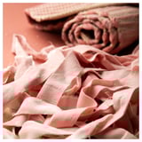 Pink woven fabric scraps, some rolled, others flat, on a peach background. Handmade, unique design.