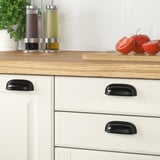 Wood kitchen counter with black cup handles, used for holding condiments and cutting tomatoes.