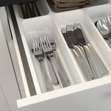 Organized cutlery drawer with forks, knives, spoons in compartments.