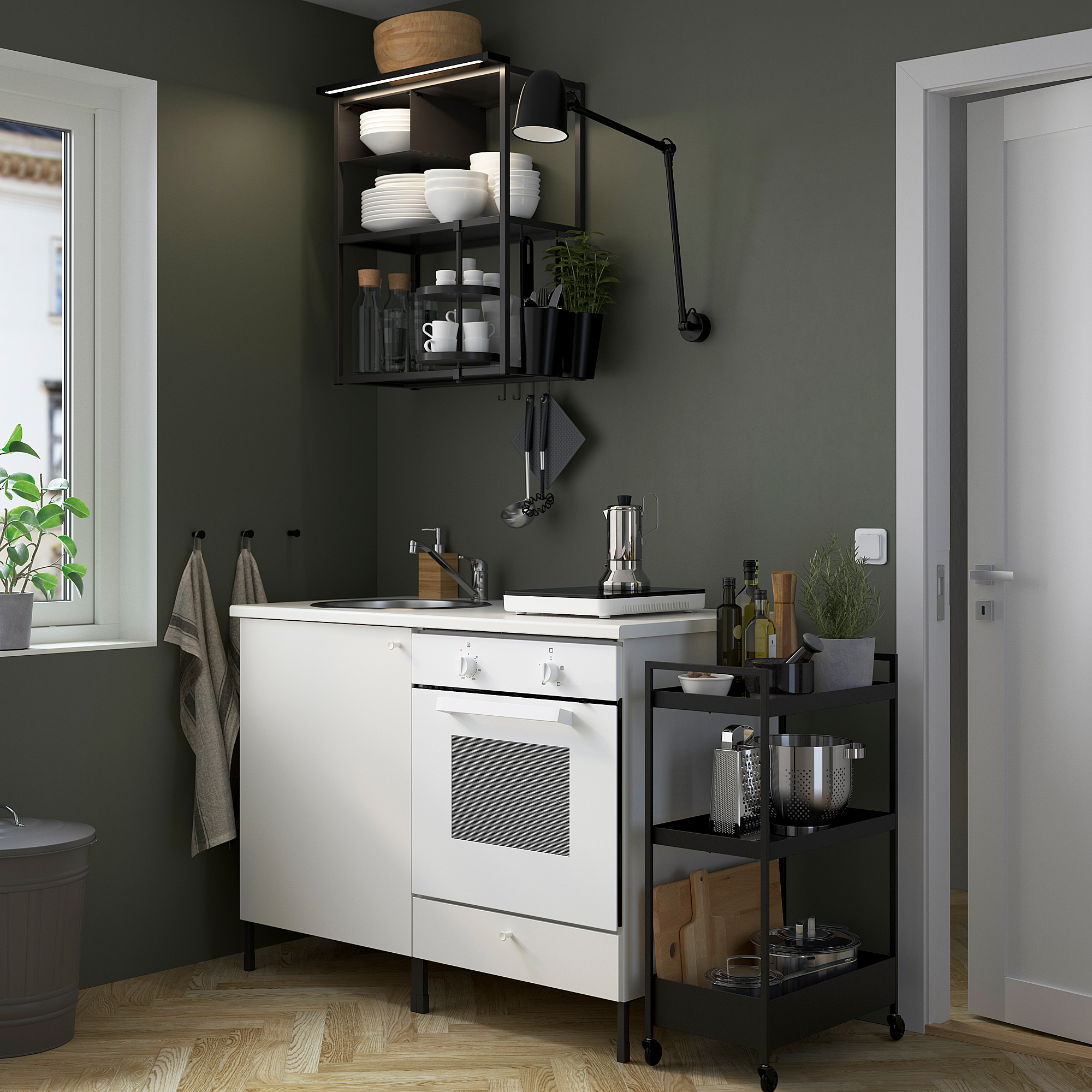 Modern compact kitchen with white cabinets, stainless steel sink, dishes on open shelves, and wooden floor.