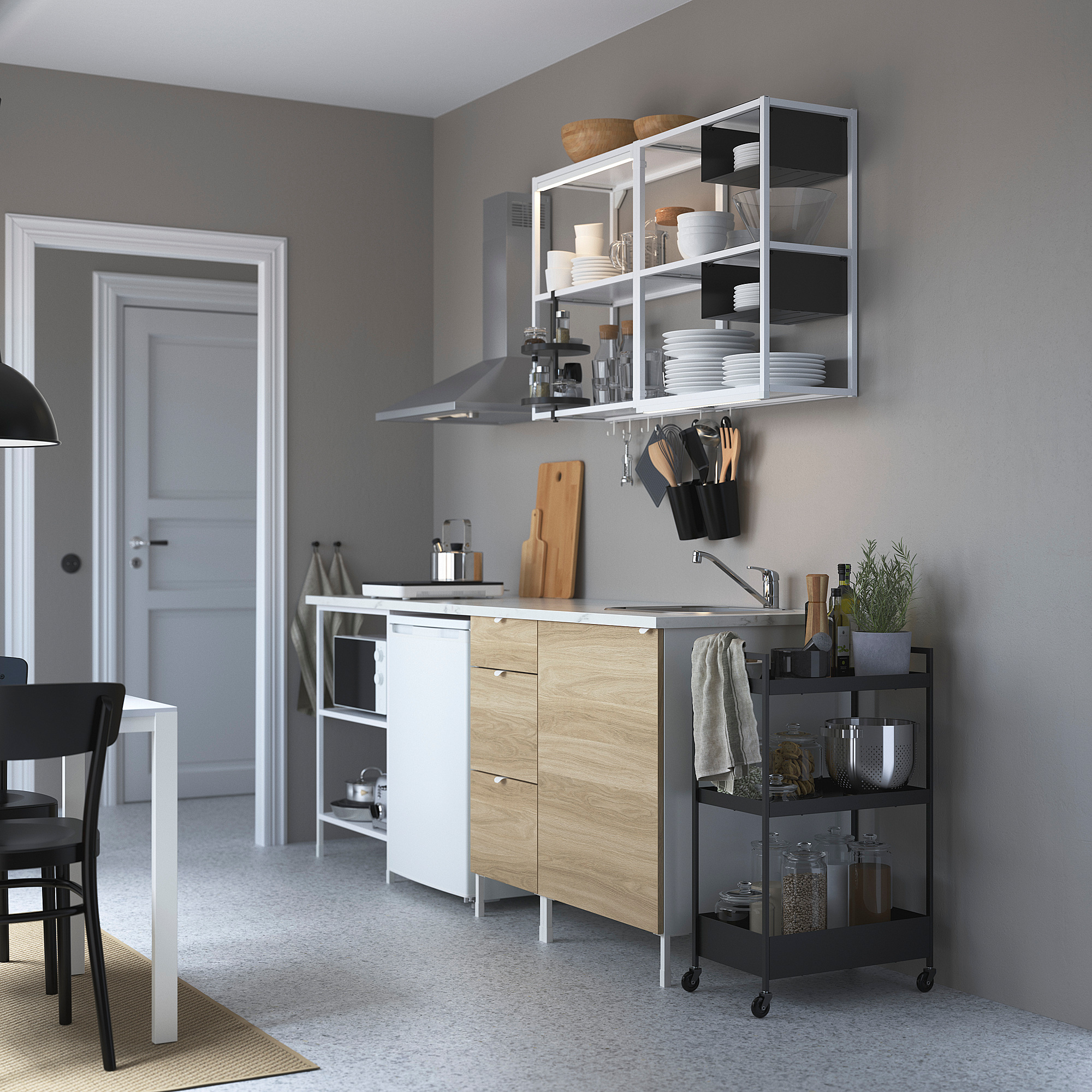 Modern kitchen with grey cabinets, stainless steel hood, white dishes, wooden island drawers, and storage cart.