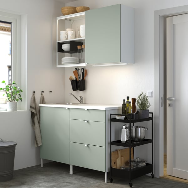 ENHET kitchen: green base cabinet with drawers, wall & open storage, single-bowl sink, rolling cart with items.