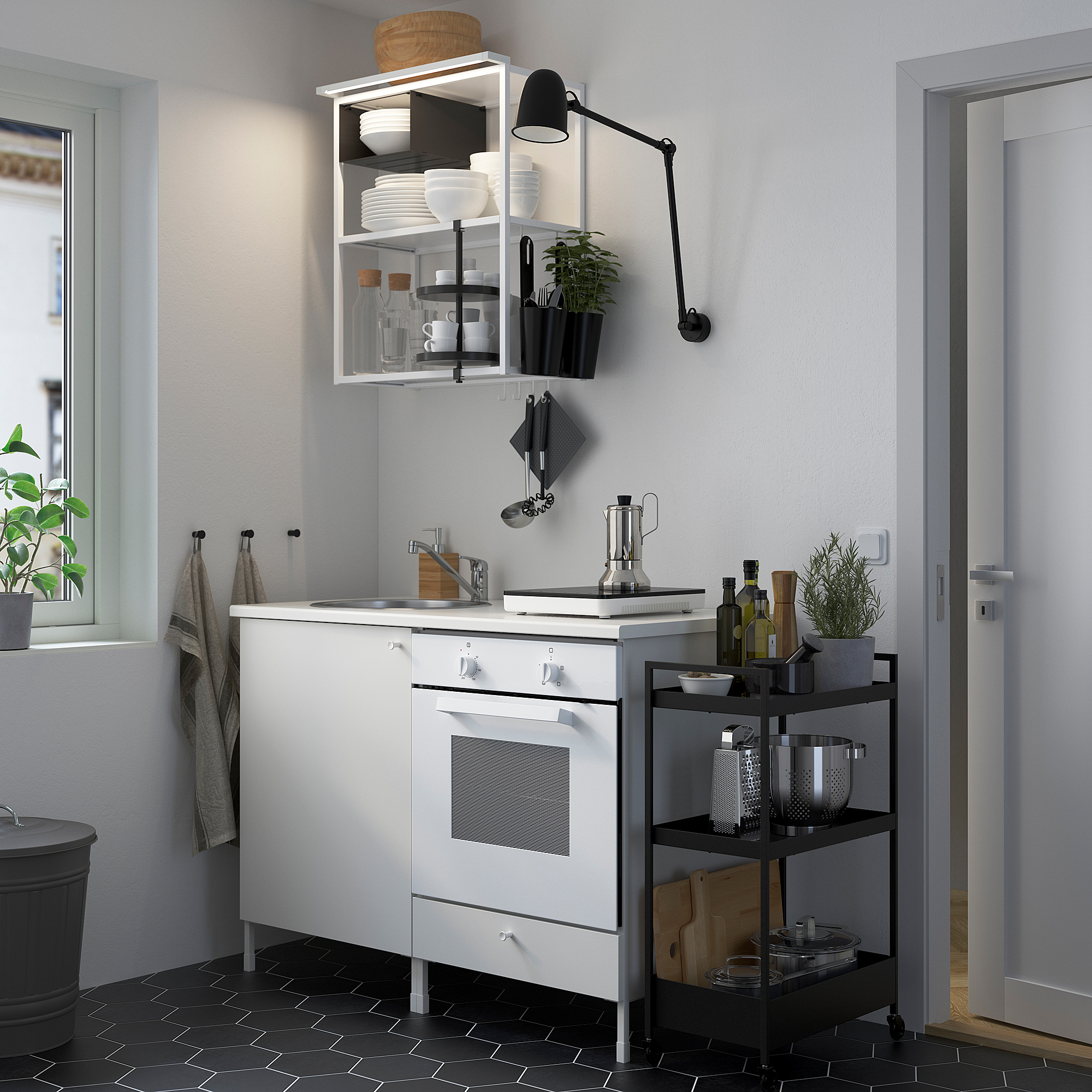 Modern kitchen setup with white ENHET units, narrow black-tiled floor, integrated appliances, open shelving, and wall-mounted light.