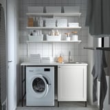Modern laundry room with white ENHET unit. Counter, sink, washing machine, and storage shelves.