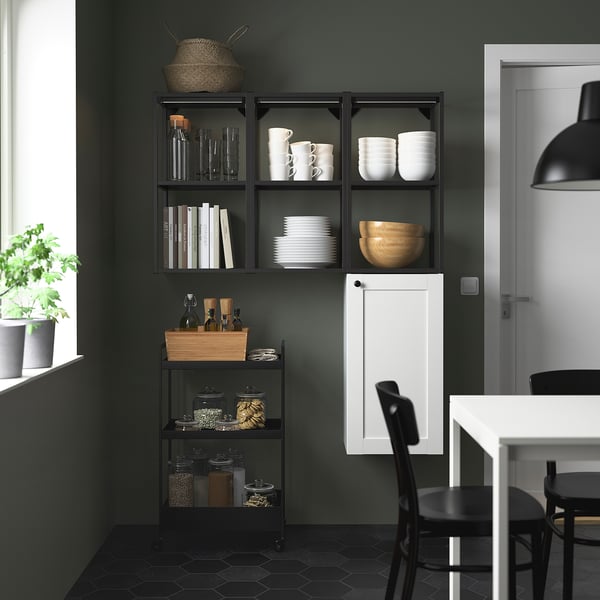 Modern kitchen with ENHET black shelves displaying dishes, books, and jars next to white cabinet and black chair.