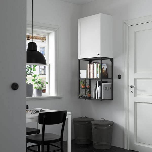 Minimalist storage: white ENHET cabinet, black shelf with plants, books, and bins. Desk with two chairs nearby.