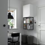 Minimalist storage: white ENHET cabinet, black shelf with plants, books, and bins. Desk with two chairs nearby.