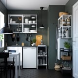 Modern kitchen with white ENHET cabinets, black appliances, and green walls, featuring open and closed storage solutions.