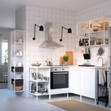Modern white kitchen with high and open shelving, black lamp shades, stainless steel stove, and various cooking tools.