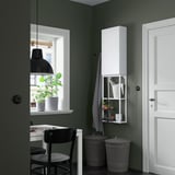 Modern green room corner with tall white cabinet, small desk, chair, and two grey bins.