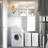 Modern minimalist laundry room with white ENHET storage, washing machine, towels, and baskets. Clean, organized with glossy surfaces.