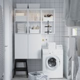 Modern white ENHET laundry unit; large cabinet, open shelves, washing machine, black stool, basket, clean design.