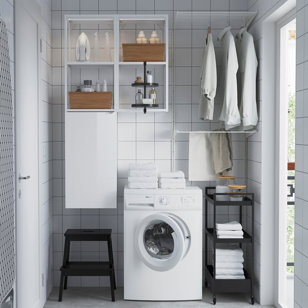 Modern laundry setup: ENHET white washing machine, black stool, open storage with laundry items.