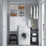 Modern laundry setup: ENHET white washing machine, black stool, open storage with laundry items.
