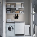 Modern laundry room with ENHET white cabinet, washing machine, shelves, gray walls, and organized storage.