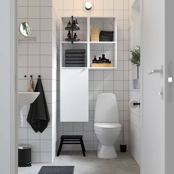 Modern bathroom with ENHET shelves, white/to gray tiles, toilet, sink, black stool, mirror, plant.