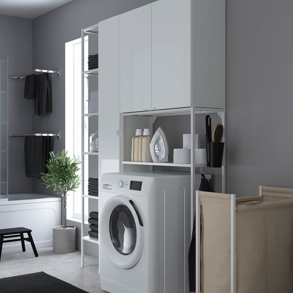 Modern grey laundry area with ENHET white cabinet, washing machine, shelves, and hanging towels. Space-efficient design.