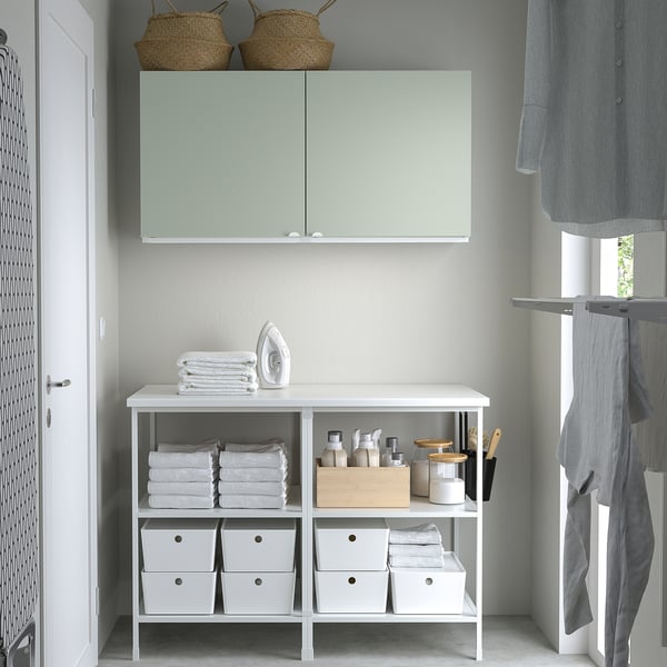 ENHET white wall cabinet with greenish doors, wicker baskets, iron, folded towels, and storage boxes. Size: large, above counter height.