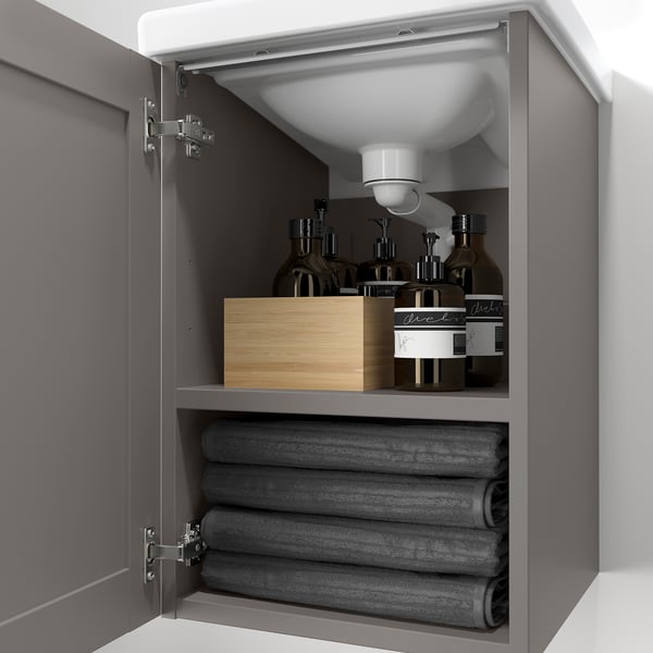 Open grey bathroom cabinet, displaying grey towels below and toiletries on top, depicting storage functionality.