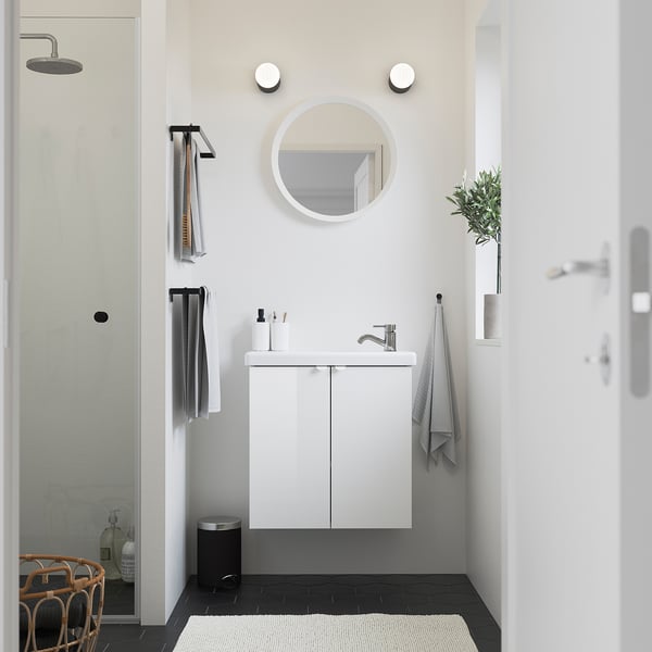 Modern minimalist bathroom with ENHET vanity, mirror, sink, and towel racks. Glass shower, black floor. Narrow, deep cabinet for small bathrooms.