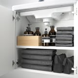 Open white bathroom cabinet with neatly folded gray towels and brown bottles on shelves.