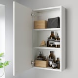 Open white cabinet displays bottles, brush, and boxes on three shelves. Timeless design with a wide frame.