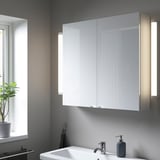 A modern bathroom with a large glossy ENHET cabinet between lights, a white sink, and a gray soap dispenser, exuding order and calm.