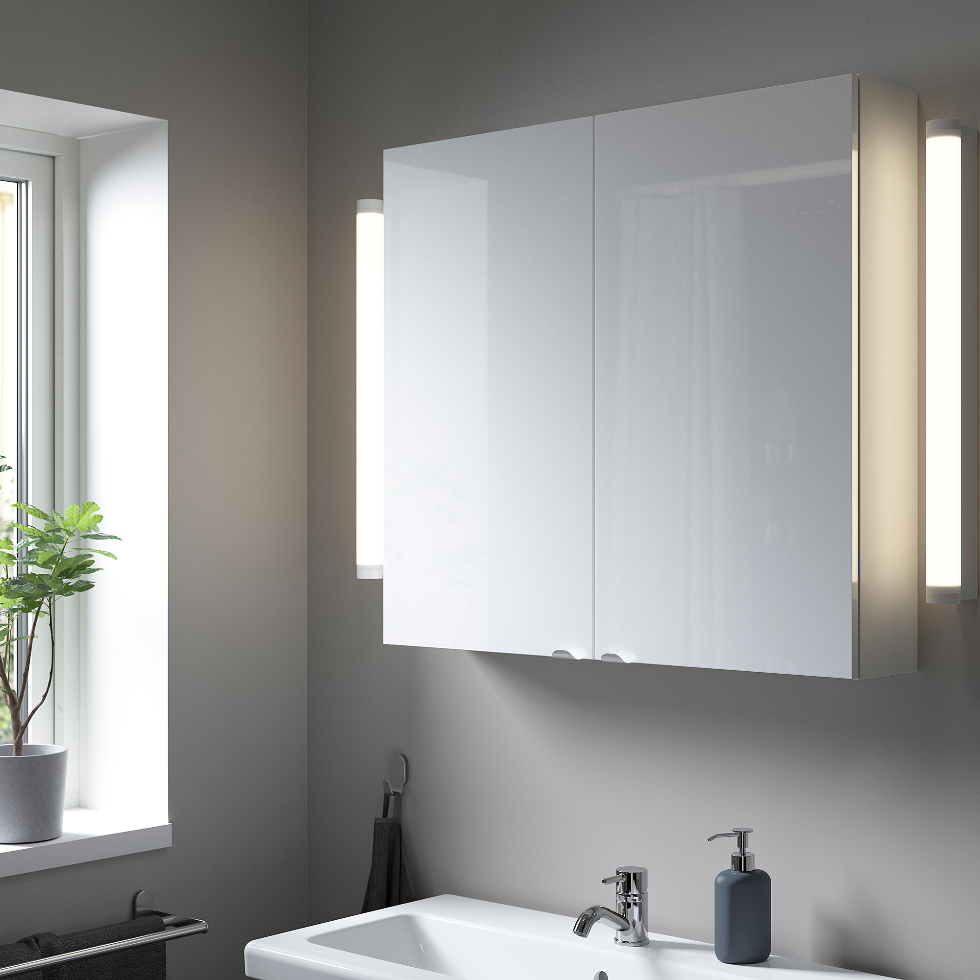 A modern bathroom with a large glossy ENHET cabinet between lights, a white sink, and a gray soap dispenser, exuding order and calm.