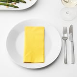 White dinnerware with yellow napkin, fork, knife, glass, and asparagus.