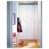 A modern wardrobe with white high-gloss doors, a coat rack with clothes, and a small stool with a red bag.