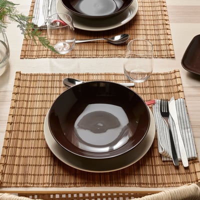Table set with FÄRGKLAR deep plates, utensils, and glassware on bamboo mats.