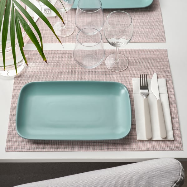 Top view of a table with two light blue rectangular plates and wine glasses, surrounded by placemats and cutlery.
