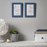 Blue frames on gray wall over desk with plant, elephant, lamp.