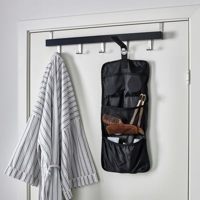 Black FODERSKOPA cable organizer hangs on wall; holds small items, near striped towel.
