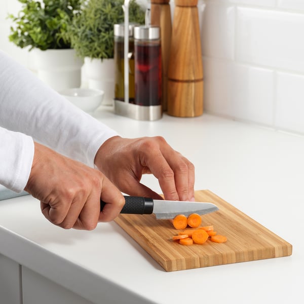 Person prepares vegetables using a FÖRSLAG knife on a wooden cutting board.