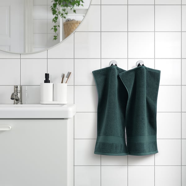 Dark green FREDRIKSJÖN towel hangs near a modern bathroom sink, larger than nearby toothbrushes.