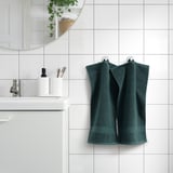 Dark green FREDRIKSJÖN towel hangs near a modern bathroom sink, larger than nearby toothbrushes.