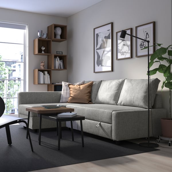 Modern living room with grey convertible sofa, wooden tables, bookshelf, and large window. Sofa is main focus with cushions.