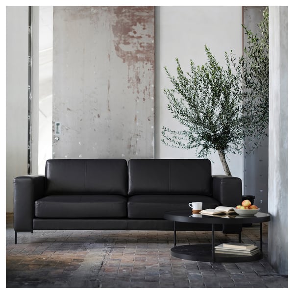 Modern living room: grey sofa, black coffee table, olive tree, industrial decor.