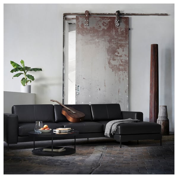 Modern living room black leather l-shaped FULLERÖ sofa with wooden guitar, black coffee table, and tall red vase.